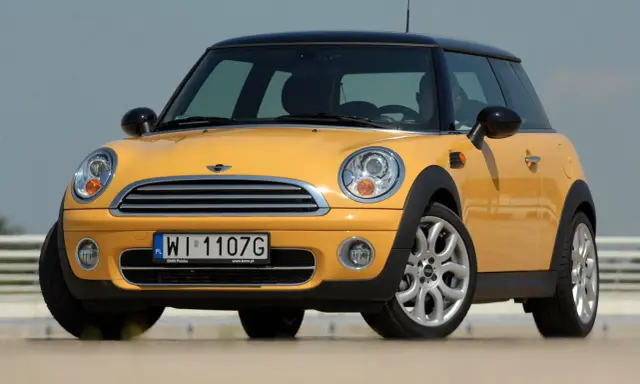 Żółty Mini Cooper, jedna z nowszych generacji, z czarnym dachem i felgami.