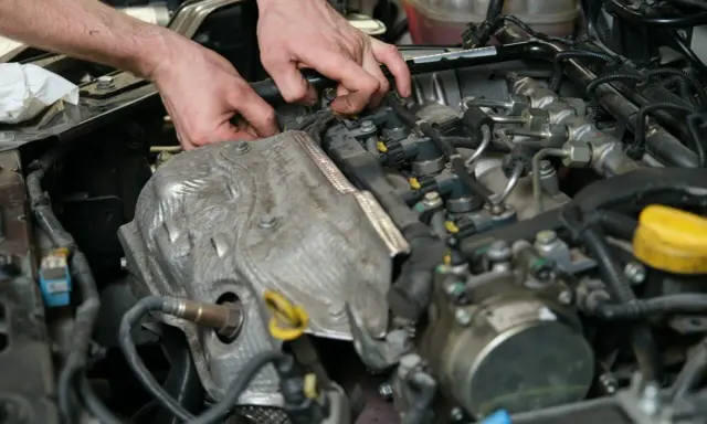 Mechanik pracuje przy silniku, sprawdzając czujnik wałka rozrządu. Objawy jego awarii mogą być różne.
