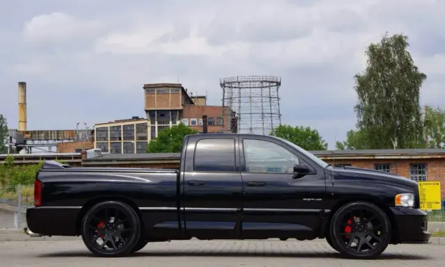 Czarny Dodge Ram 1500 SRT-10, potężny pickup, prezentuje swoje imponujące ramiona na tle postindustrialnego krajobrazu.
