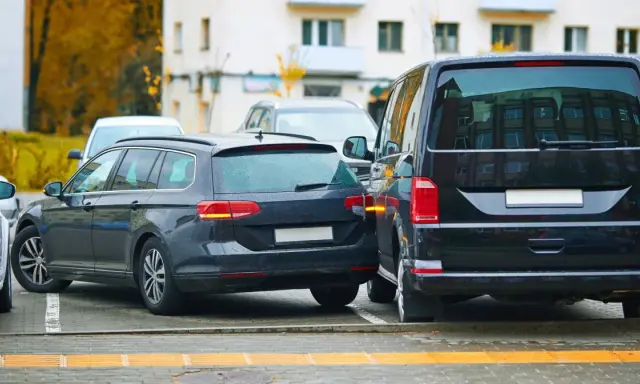 Ciemny kombi zaparkowany zbyt blisko drugiego samochodu, ledwo mieszcząc się na miejscu parkingowym.