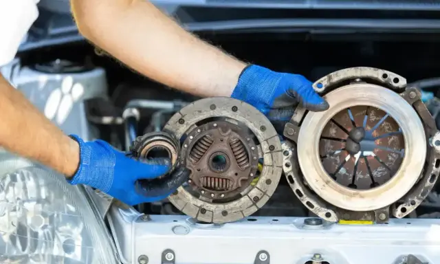 Mechanik w niebieskich rękawiczkach trzyma części samochodowe. Wygląda na to, że właśnie wymienia ślizgające się sprzęgło.