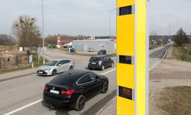Żółty fotoradar przy drodze, monitorujący ruch samochodów. Tak działa system, który rejestruje prędkość pojazdów.