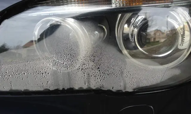 Zaparowany reflektor od środka, z licznymi kropelkami wody na kloszu.
