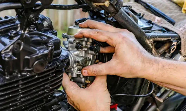 Ręce mechanika regulują gaźnik motocykla, pokazując, jak działa ssanie.