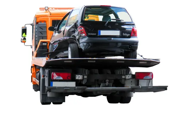 Pomoc drogowa pokazuje, jak holować auto po wypadku. Uszkodzony czarny Renault Twingo jest ładowany na lawetę.