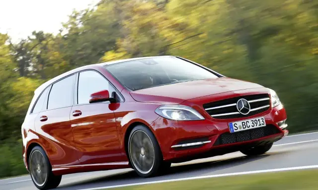 Czerwony Mercedes Klasy B w ruchu, z rozmytym tłem drzew i drogi.