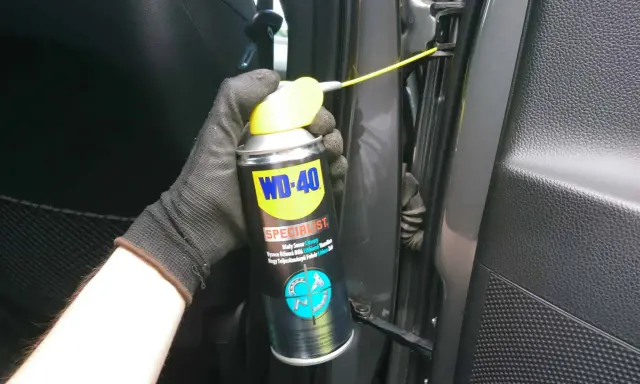 Ręka w rękawiczce aplikuje smar do zawiasów drzwi samochodowych WD-40 Specialist.