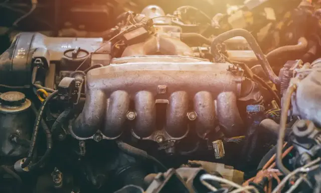 Silnik samochodowy z widocznym, zakurzonym kolektorem ssącym. Widać przewody i inne elementy mechaniczne.