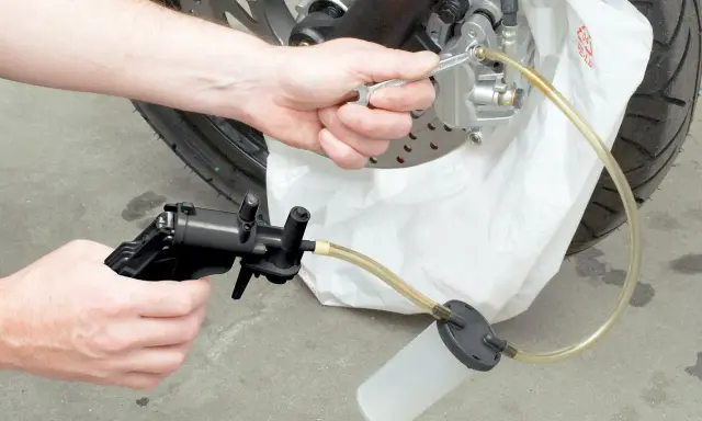 Ręce majsterkowicza odkręcają odpowietrznik zacisku hamulcowego, przygotowując się do tego, jak wymienić płyn hamulcowy w motocyklu.
