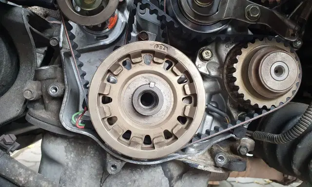 Zbliżenie na mechanizm silnika, widoczne koła zębate i pasek. Przygotowanie do wymiany rozrządu.