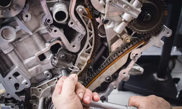 Mechanik naprawia rozrząd silnika. Luźny łańcuch może być jednym z objawów zużytej poduszki silnika.