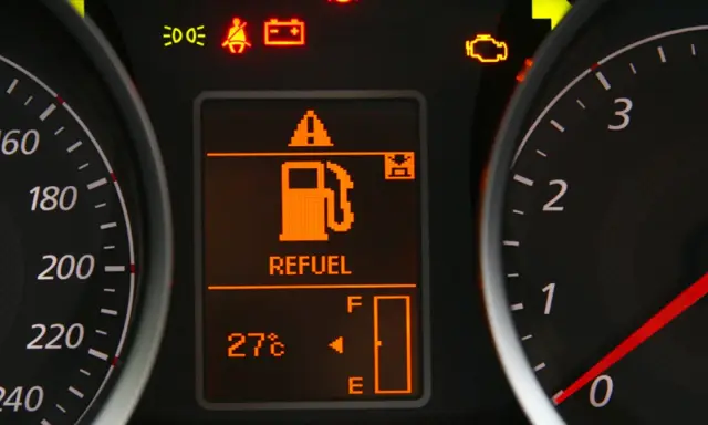 Na desce rozdzielczej świeci się kontrolka paliwa z napisem "REFUEL". Wskaźnik pokazuje niski poziom paliwa, sugerując, że rezerwa ile km zostało do przejechania jest niewielka.