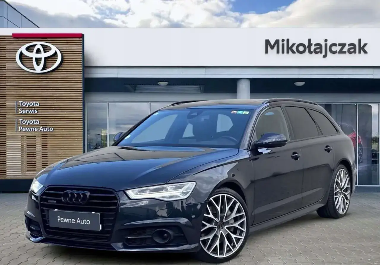 Ciemny Audi A6 C7 kombi, model z lat produkcji 2011-2018, zaparkowany przed salonem samochodowym.