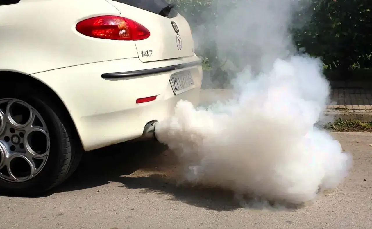 Biały dym wydobywa się z rury wydechowej białego samochodu Alfa Romeo 147.