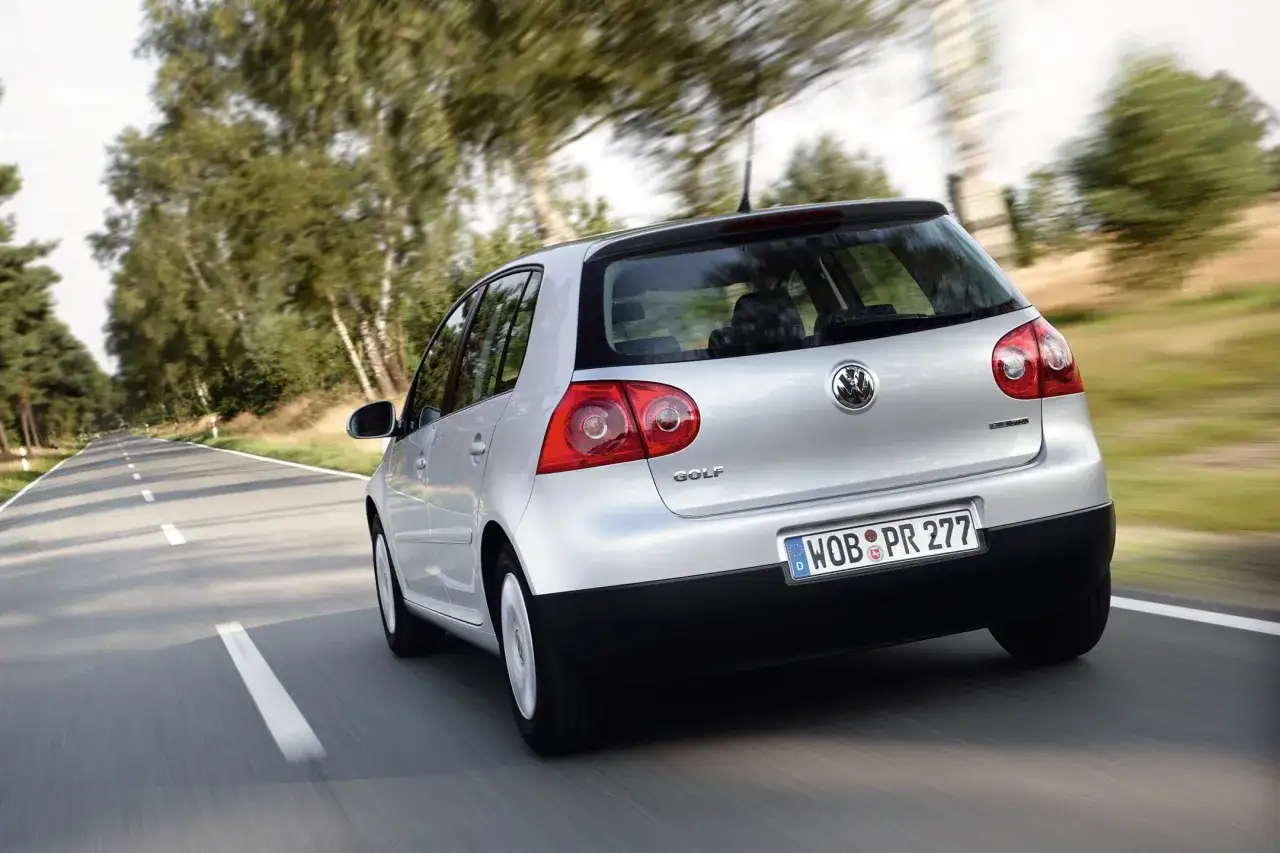 Srebrny Golf 5 1.6 MPI pędzi po wiejskiej drodze, otoczony zielenią drzew.