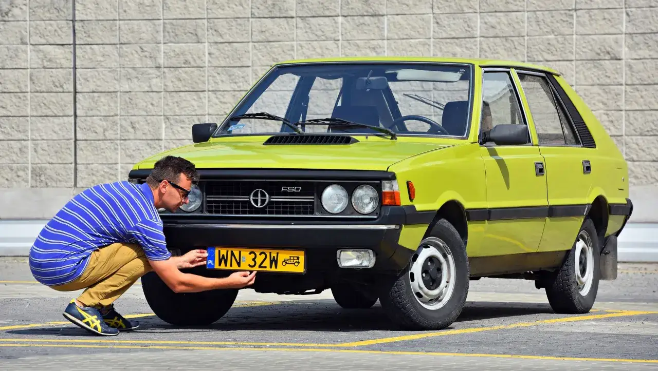 Mężczyzna montuje żółtą tablicę rejestracyjną do zielonego Poloneza. To ważny krok, by zarejestrować auto na zabytek.