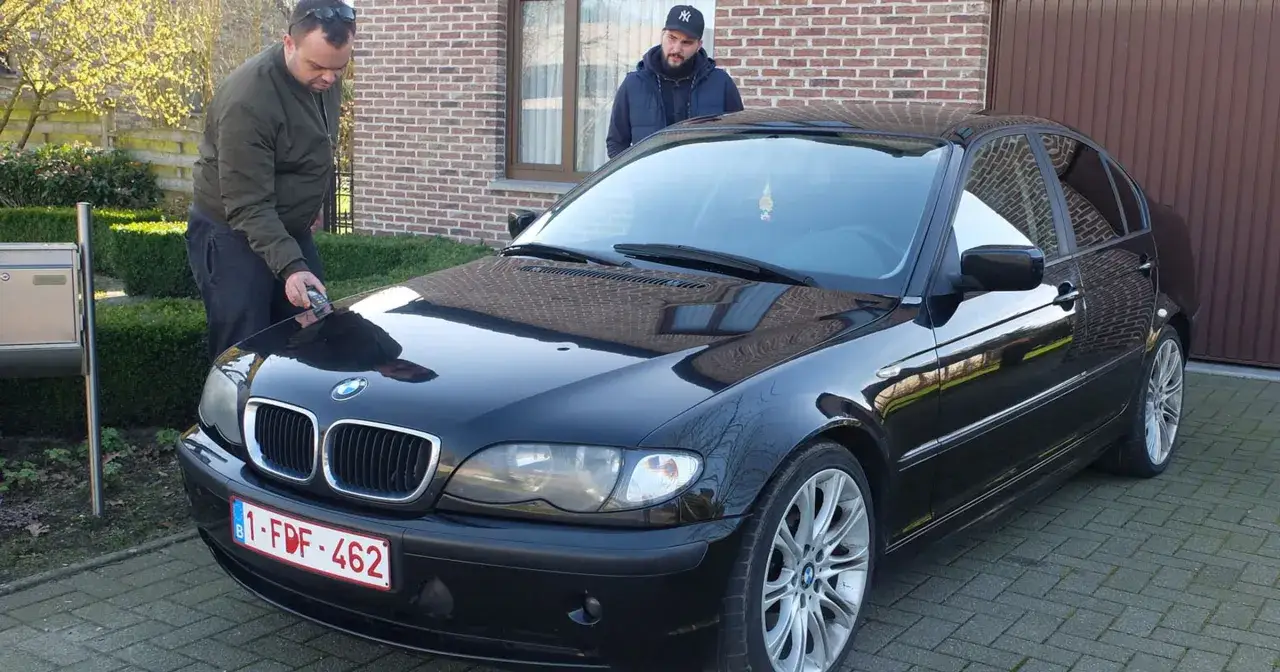 Mężczyzna sprawdza czarny BMW, marząc o bezawaryjnych autach. Obok stoi drugi mężczyzna.