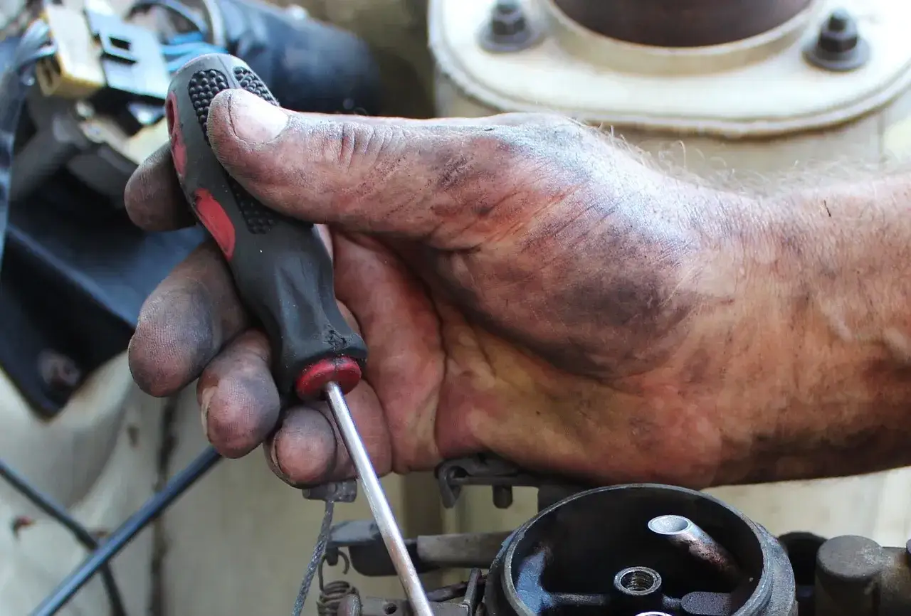 Brudna ręka mechanika reguluje linkę sprzęgła z samoregulatorem, pokazując zasadę działania mechanizmu.
