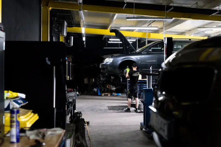 Mechanik bada przyczynę, dlaczego auto nie odpala. Podniesiony przód pojazdu i widoczny silnik sugerują skomplikowaną usterkę.